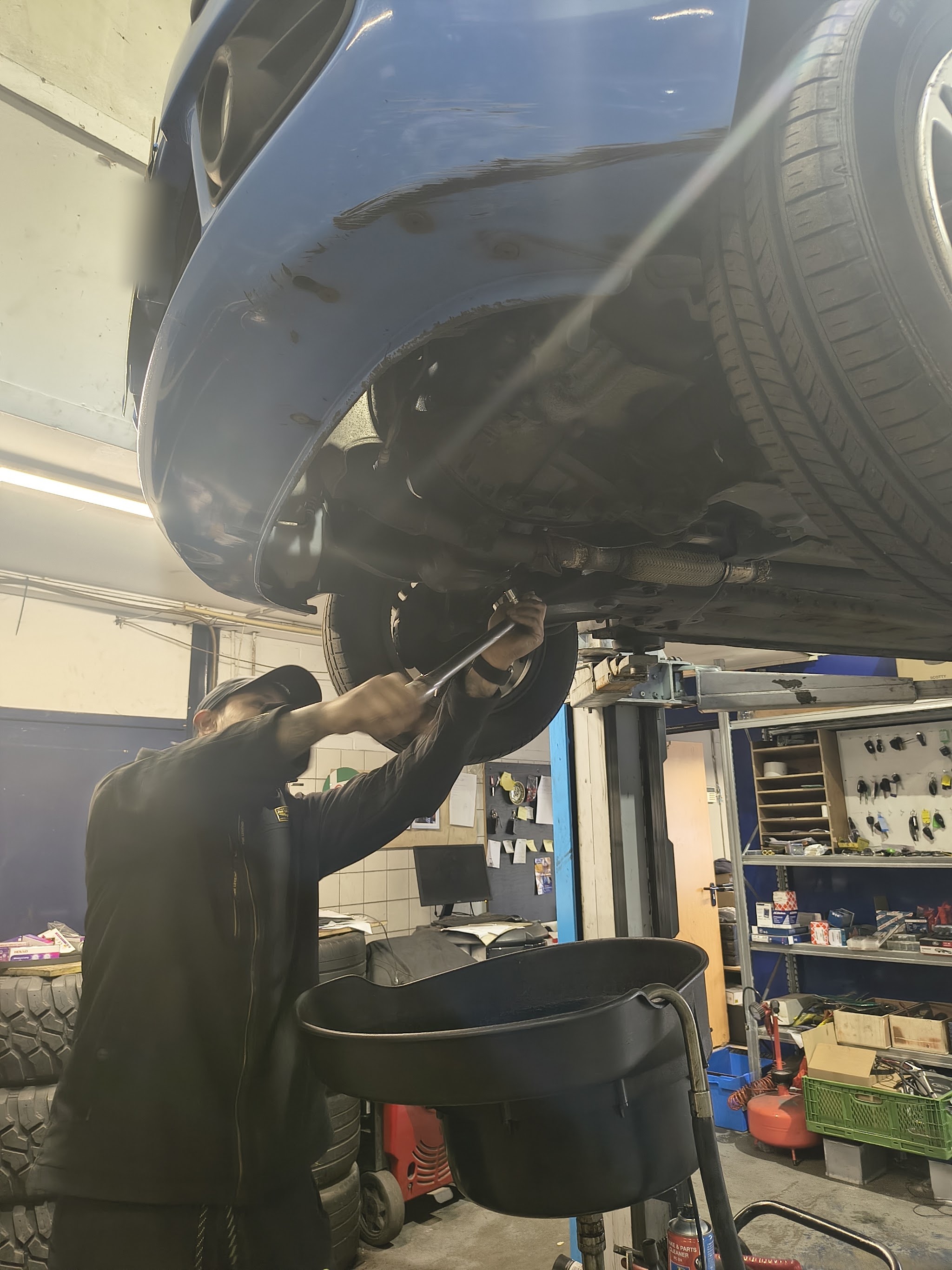 Een monteur onder een opgetilde auto met gereedschap en onderdelen in de werkplaats